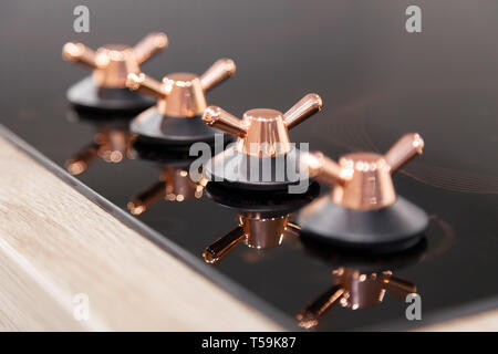 Closeup of the copper knob switch plates are reflected in the black shiny electric or gas hob for the kitchen. Concept of modern household appliances  Stock Photo