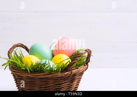 Easter wicker basket with colored pastel eggs decoration. Copy space. White wooden background. Selective focus. Easter holiday concept Stock Photo
