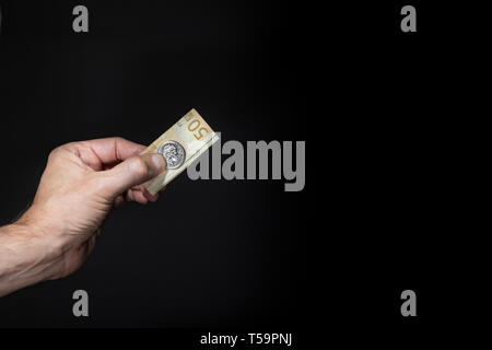 Male hand holding a five pence coin with the image of Elizabeth II  and a 50 euros banknote, isolated over black, brexit concept. Stock Photo