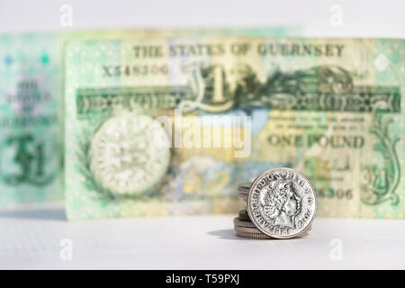 A five pence coin with the image of Elizabeth II over a blurred banknote from Guernsey. Stock Photo