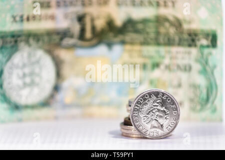 A five pence coin with the image of Elizabeth II over a blurred banknote from Guernsey. Stock Photo