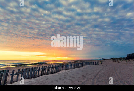 Fence on sand beach at sunset in Chipiona, Andalusia. Footprints in sand. Vacation travel background Stock Photo