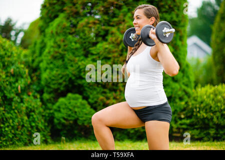 Pregnant Woman Doing Kneeling Lunges With Dumbbells In Park Stock Photo