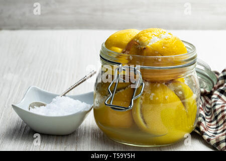 Moroccan  preserved salted lemons in glass jar on white wooden table Stock Photo