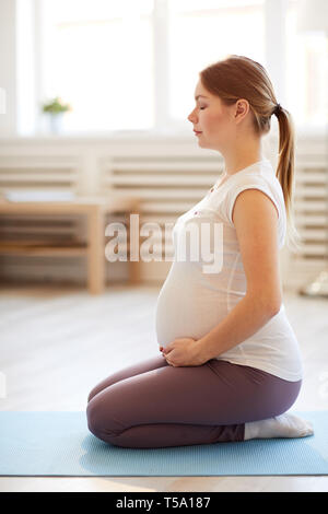 Portrait of young pregnant woman doing yoga on mat with online video ...