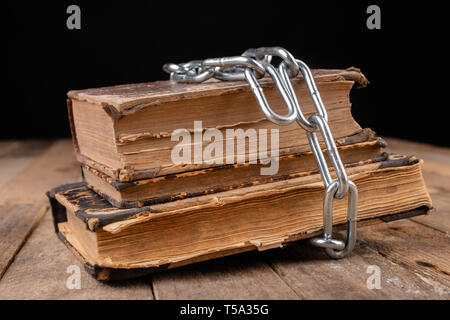 Old books related to a new shiny chain. Forbidden old works artists on a wooden table. Dark background. Stock Photo