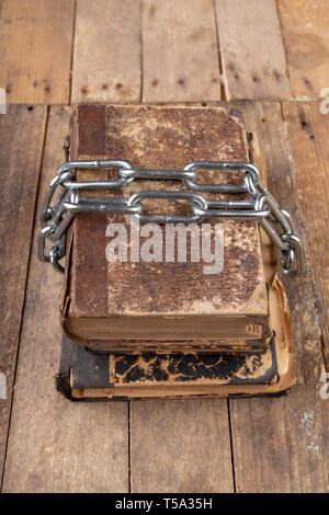 Old books related to a new shiny chain. Forbidden old works artists on a wooden table. Dark background. Stock Photo