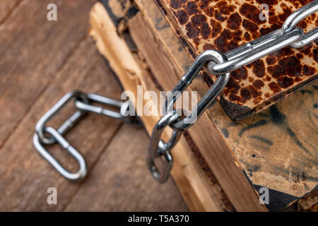 Old books related to a new shiny chain. Forbidden old works artists on a wooden table. Dark background. Stock Photo