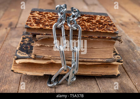 Old books related to a new shiny chain. Forbidden old works artists on a wooden table. Dark background. Stock Photo