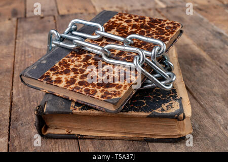 Old books related to a new shiny chain. Forbidden old works artists on a wooden table. Dark background. Stock Photo