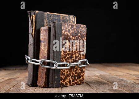 Old books related to a new shiny chain. Forbidden old works artists on a wooden table. Dark background. Stock Photo