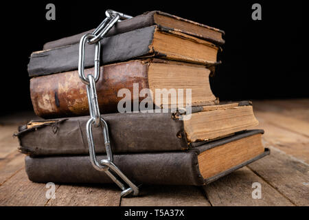 Old books related to a new shiny chain. Forbidden old works artists on a wooden table. Dark background. Stock Photo