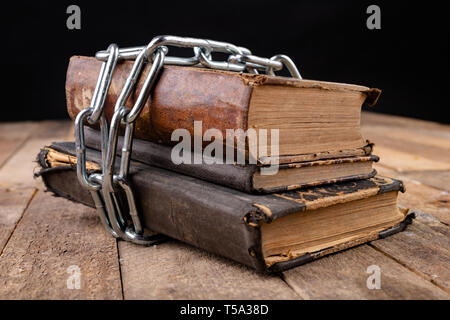 Old books related to a new shiny chain. Forbidden old works artists on a wooden table. Dark background. Stock Photo