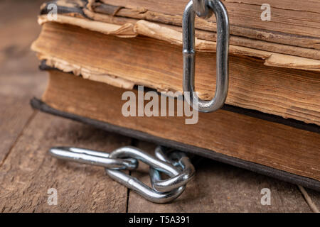 Old books related to a new shiny chain. Forbidden old works artists on a wooden table. Dark background. Stock Photo