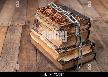 Old books related to a new shiny chain. Forbidden old works artists on a wooden table. Dark background. Stock Photo