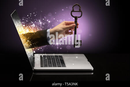 Hand with huge vintage key coming out of a laptop with sparkling effects  Stock Photo