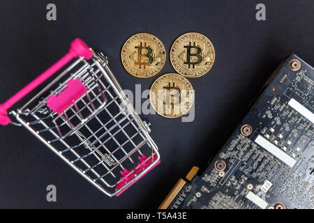 Stack of coins bitcoin in mini shopping cart toy on the video card, concept of mining. Electronic virtual money for web banking and international netw Stock Photo