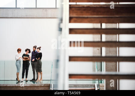 A group of young businesspeople standing near staircase, talking. Stock Photo