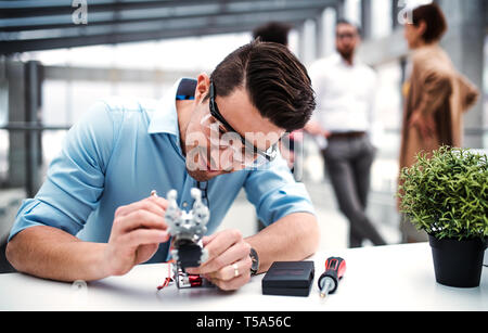 A young businessman or scientist with robotic hand and safety glasses standing in office, working. Stock Photo