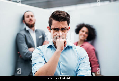 A portrait of young thoughtful businessman standing in office, colleagues in the background. Stock Photo