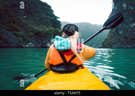 Girl kayaking on the seaside of Halong bay in Vietnam. Woman rowing oars in the boat. The view from the back. Stock Photo