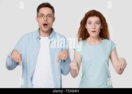 Shocked couple isolated on studio background point down Stock Photo
