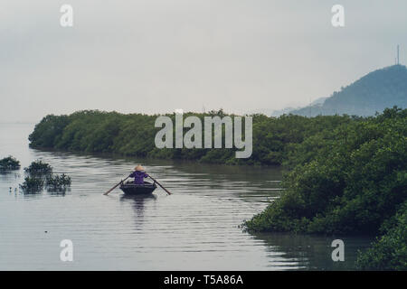 Vietnamese old women on traditional boat paddling by yellow brown water in canal. Vietnam Stock Photo