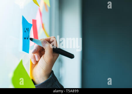 Businesswoman writing on colorful sticky note paper in business office, close up of hand