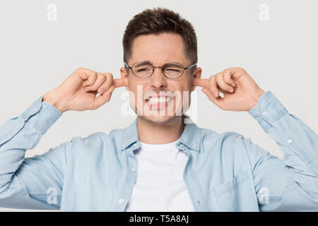 Annoyed man in glasses cover ears avoiding loud sound Stock Photo