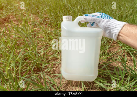 Farmer holding insecticide jug in wheatgrass field, blank plastic ...