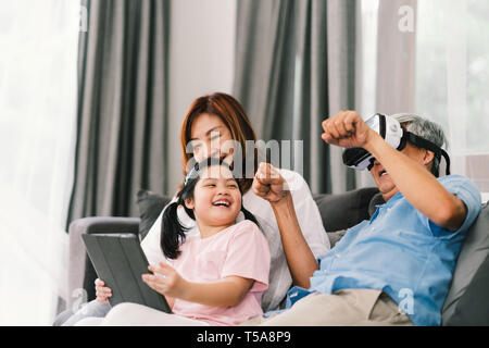 Lovely happy people playing Virtual Reality game together, young kid girl using digital tablet, grandfather wearing VR headset. Family life concept Stock Photo