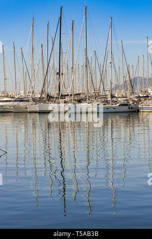 CANNES, FRANCE - APRIL 2019: Sailing boats moored close together in the harbour in Cannes, with reflections of the masts in the water. Stock Photo
