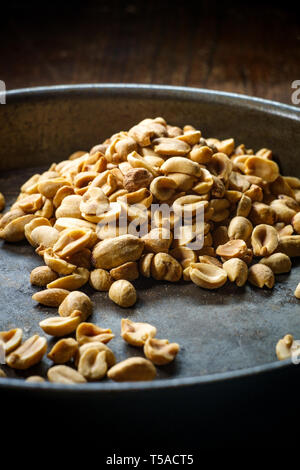 Shelled salty pub peanuts on wooden bar table and dark moody lighting Stock Photo