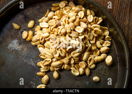 Shelled salty pub peanuts on wooden bar table and dark moody lighting Stock Photo