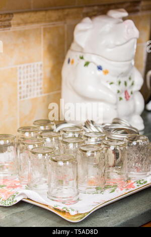 Empty upside-down clean canning jars on a tea towel which will soon be filled with apricot jam, with a pig-shaped cookie jar in the background Stock Photo