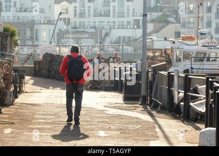 A man walks towards a group of fishermen preparing their nets on a bright early morning, Brixham Harbour, Devon, UK. Stock Photo