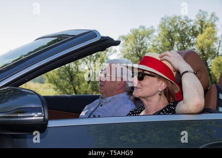 Happy older couple drives with a luxury convertible car Stock Photo