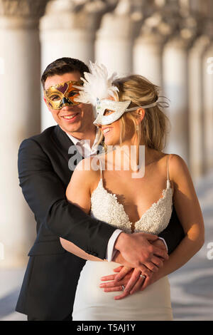 Happy smiling wedding couple, bride and groom wearing carnival masks, outdoor portrait, Venice, Italy Stock Photo