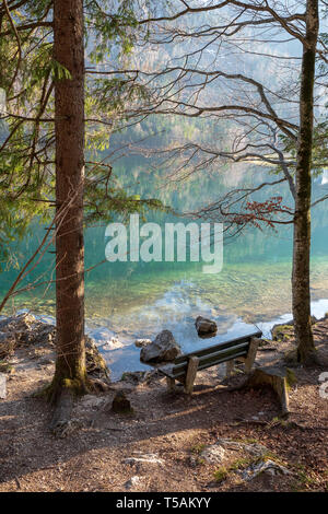 Empty wooden bench at the shore of the Vorderer Langbathsee near Ebensee, OÖ, Austria, with the great landscape reflecting on the crystal clear water Stock Photo