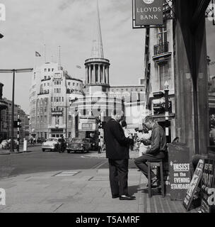 1960s, historical, Marylebone, London, at the North end of Regent Street, a gentleman buying the Evening Standard newspaper from a seller sitting on a stool under a Lloyds Bank sign. The BBC's Broadcasting House in Portland Place and All Souls Church in Langham Place also in the picture, as well as cars of the era and a No 3 Routemaster Bus heading to Crystal Palace. Stock Photo