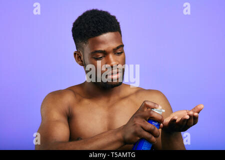 handsome young brutal man putting shaving foam on the palm, preparation for shaving, isolated in the blue background.close up photo Stock Photo