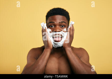 funny man with shaving foam on his face sticking out his tongue. close up photo. isolated yellow background.studio shot Stock Photo
