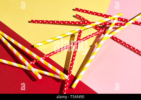 colorful plastic drinking straws isolated over the pink, yellow, red background, top view, messy table after party Stock Photo