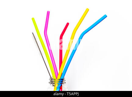 Five multicoloured reusable silicone drinking straws and their cleaning brush in a glass jar, isolated on a white background
