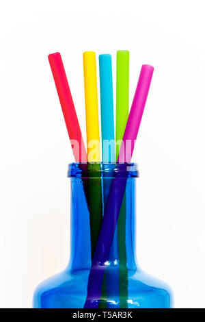 Close-up of multicoloured reusable silicone drinking straws projecting from the neck of a blue glass bottle, isolated against a white background Stock Photo