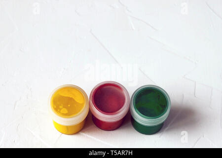 three plastic jars with multy-colored gouache or acrylic paints top cap view on a light white background. Selective soft fokus. Text copy space. Stock Photo