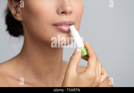 Lips nutrition. Girl applying hygienic balm over grey background Stock Photo