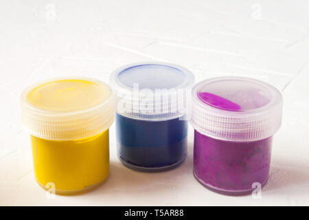 three plastic jars with multy-colored gouache or acrylic paints side view on a light white background. Selective soft fokus. Text copy space. Stock Photo