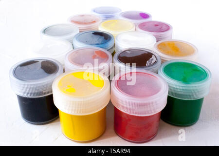 many plastic jars with multy-colored gouache or acrylic paints side view on a light white background. Selective soft fokus. Stock Photo