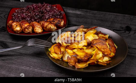 Fried potatoes and homemade grilled sausages or chevapchichi with stewed sour red cabbage on a wooden rustic background. Top view. Stock Photo